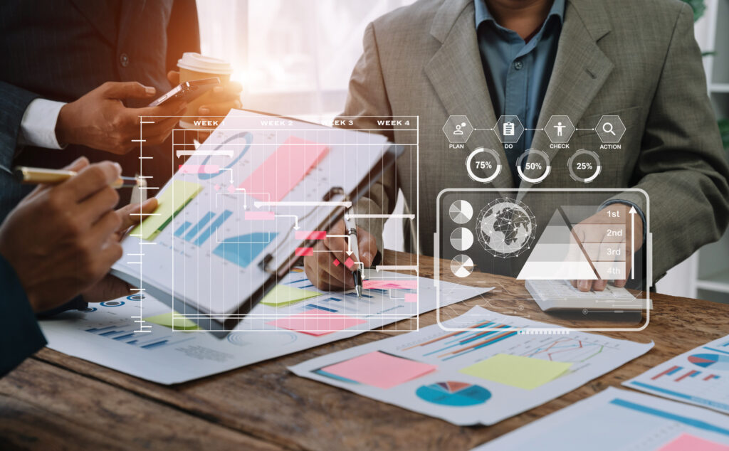 Two professionals review colorful charts and graphs on a wooden table, with a translucent data dashboard overlay lying over the scene.