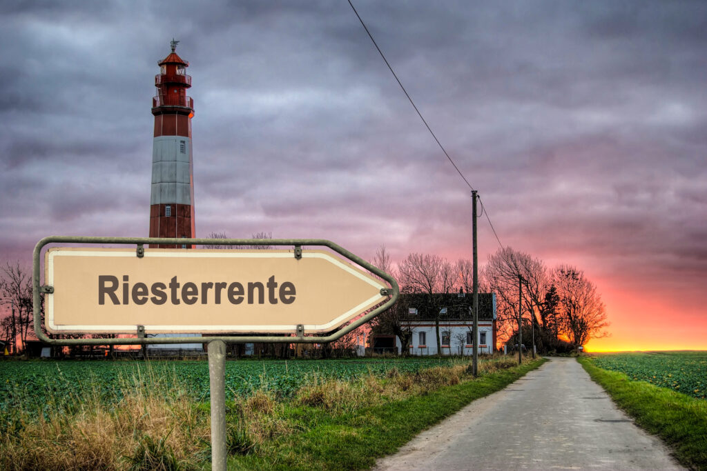 Sign in foreground reading 'Riesterente' with a red-and-white lighthouse and a sunset sky in the background