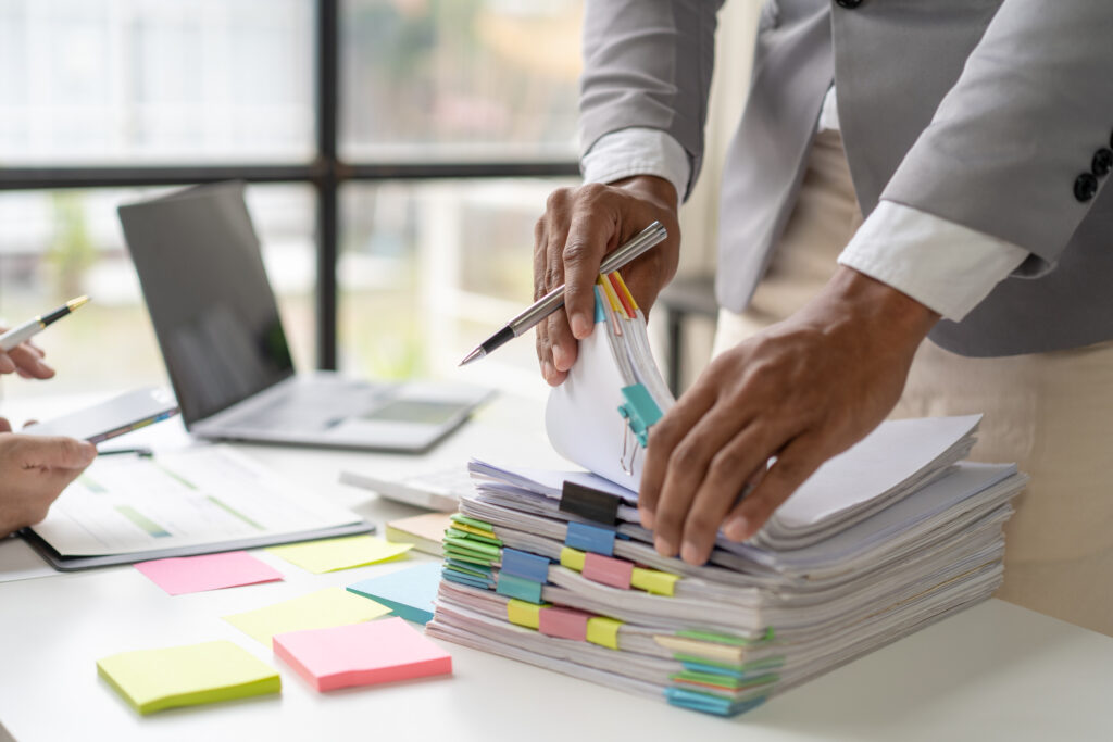 Person stacking a tall pile of papers with colorful sticky notes at a desk in an office setting to organize documents